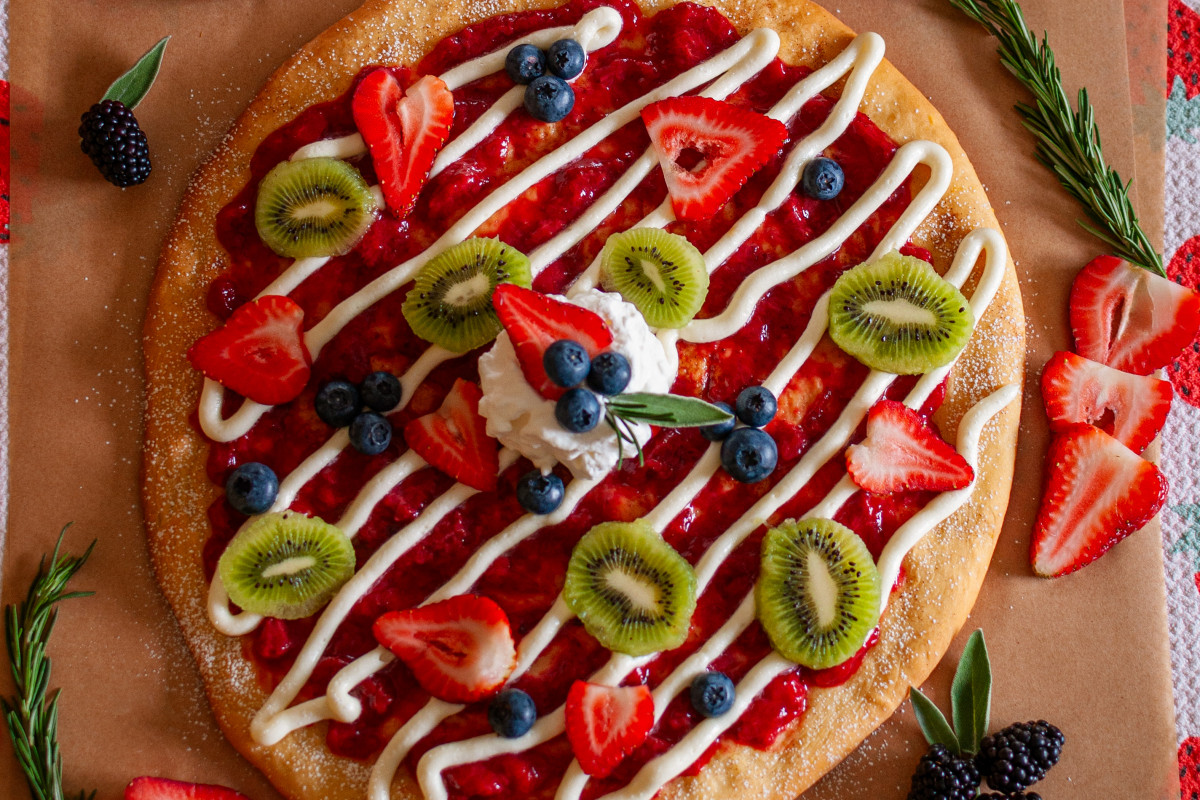 Fruit pizza with strawberry sauce, cream cheese frosting, strawberries, blueberries and kiwi slices.