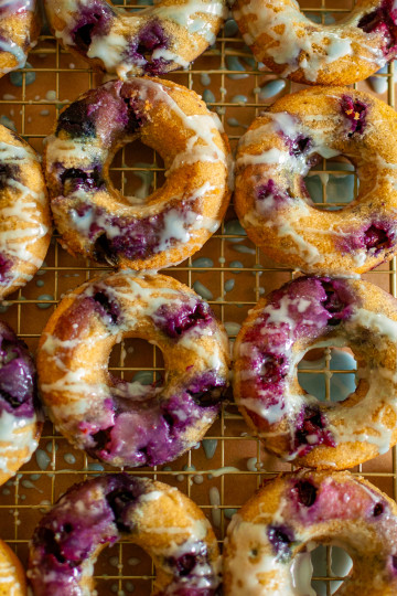 Close up shot of blueberry donuts on a cooing rack with brown parchment paper beneath them.