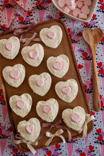 Heart shaped no-bake cheesecakes with small pink heart marshmallows on top, on a wooden board with bows decorating the board.