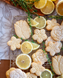 Lemon shortbread cookies cut into flower shapes with slices of lemons and thyme.