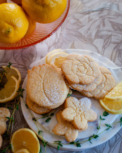 Lemon shortbread cookies cut into flower shapes with slices of lemons and thyme.