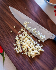 Finely chopped garlic and an 8 inch chef's knife on a wooden cutting board.