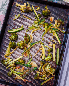 Zucchini, broccoli, and garlic on a rimmed baking sheet after roasting.
